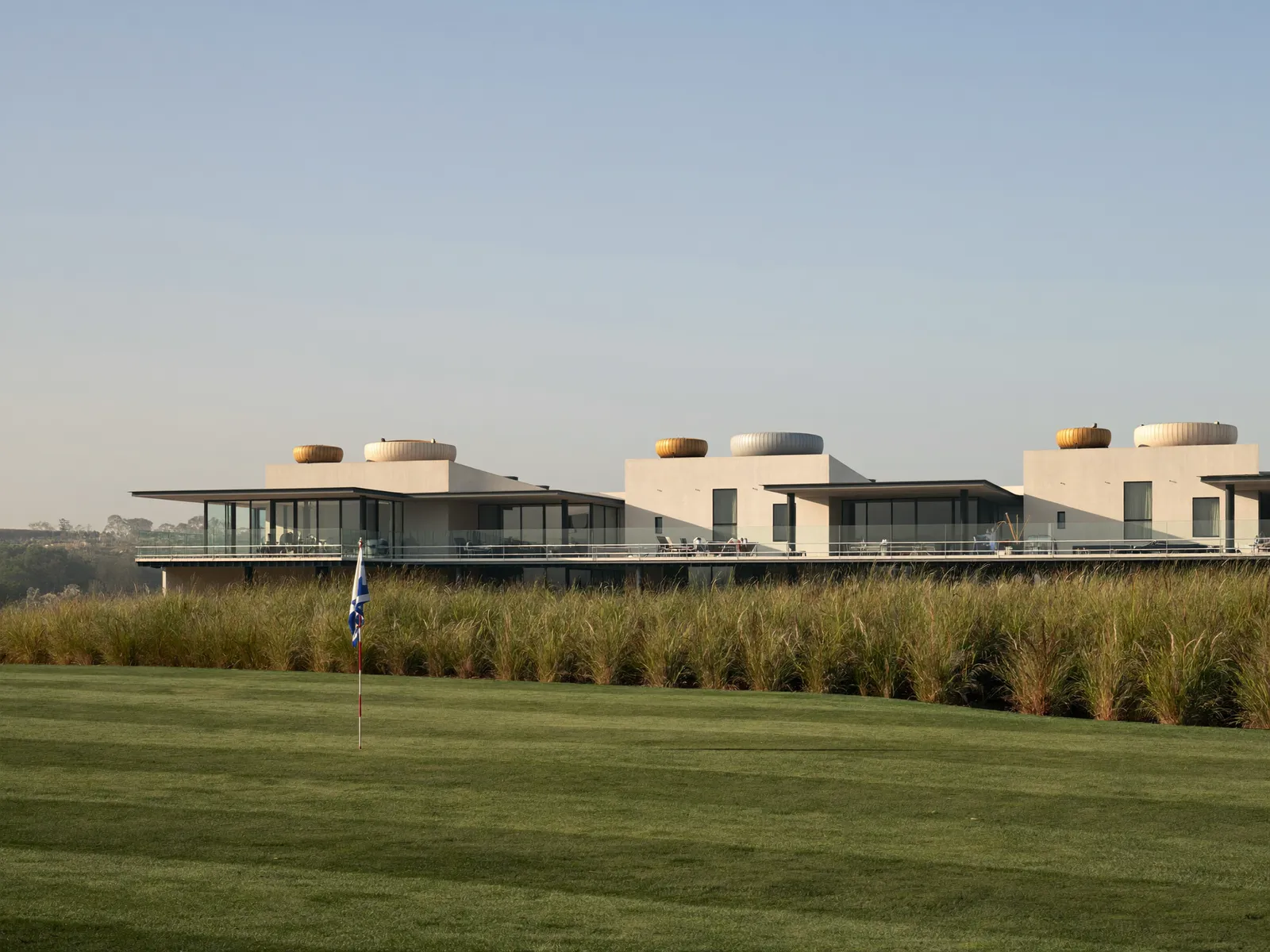 Row of townhouses in Damac Hills with small water tanks on the roofs and a golf course behind